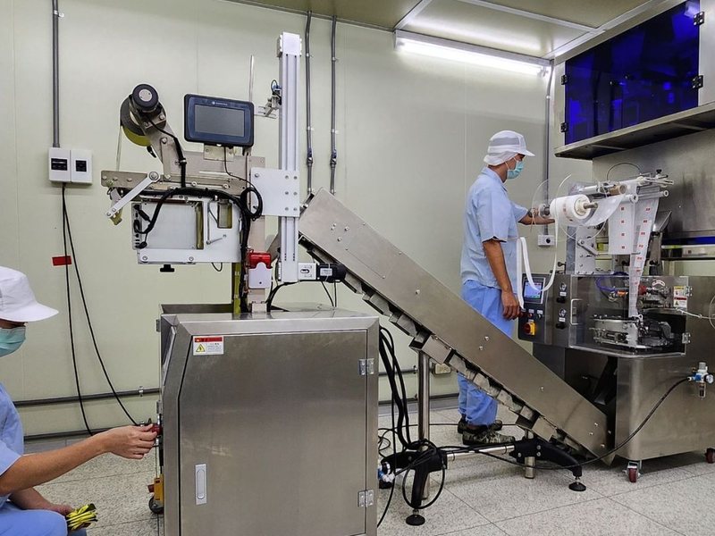 保康生醫廠內自動化包裝產線，兩名著無塵衣人員操作茶包包裝機與輸送設備
